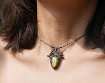 May include: A silver necklace with a teardrop-shaped gemstone pendant. The gemstone is a labradorite with iridescent green, gold, and blue hues. The pendant is surrounded by a silver wire design.