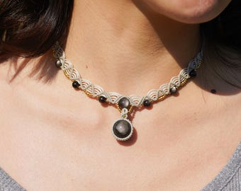 May include: A white and black macrame choker necklace with a gold accent and a round black gemstone pendant.