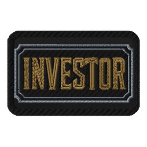 May include: Embroidered patch with the word "INVESTOR" in gold thread. The text is inside a rectangular frame with a silver border, set against a black background. The patch has a stitched edge.