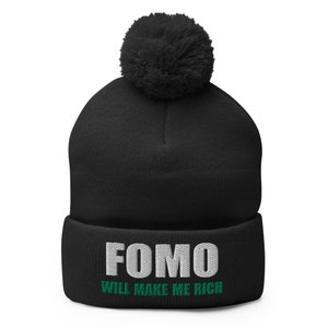 Puede incluir: Gorro negro con un pompón blanco y el texto "FOMO WILL MAKE ME RICH" en blanco y verde.