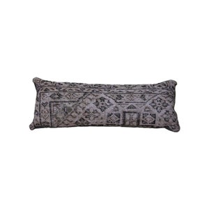 Puede incluir: Una almohada larga y rectangular con fondo beige y un patrón geométrico en blanco y negro. La almohada está hecha de una tela suave y tejida.