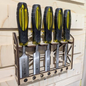 Könnte beinhalten: Ein Wandhalter aus Holz mit sechs Steckplätzen für Meißel. Der Halter ist aus hellbraunem Holz und hat einen schwarzen Metallrahmen. Die Meißel sind mit ihrer Größe in Millimetern beschriftet. Die Meißel sind gelb und schwarz.