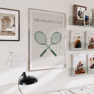 Puede incluir: Una impresi&oacute;n enmarcada con un fondo beige y el texto "THE RACQUET CLUB" en negro. Dos raquetas de tenis verdes se cruzan en el centro de la impresi&oacute;n.