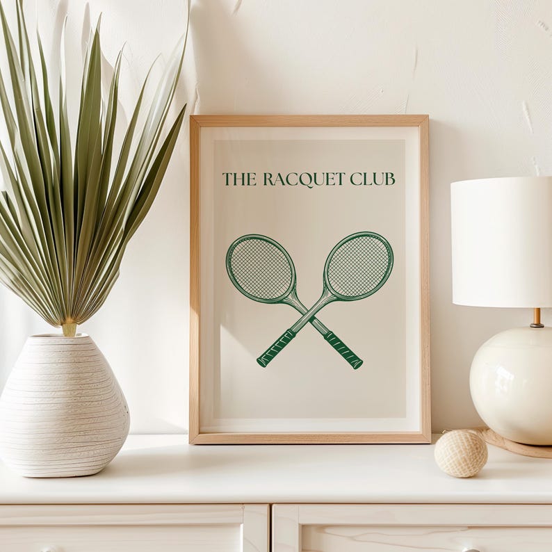 Puede incluir: Una impresi&oacute;n enmarcada con un marco marr&oacute;n claro y un fondo blanco. La impresi&oacute;n presenta una ilustraci&oacute;n verde de dos raquetas de tenis cruzadas y el texto "THE RACQUET CLUB".