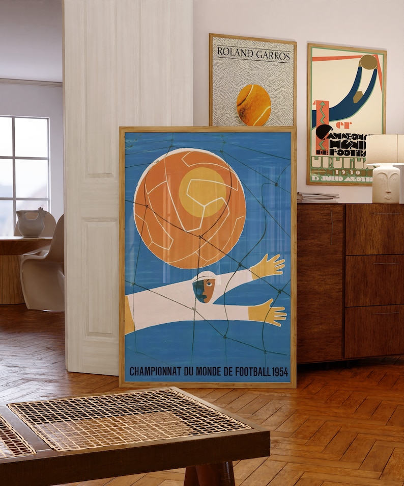 May include: A vintage poster with a blue background and a stylised illustration of a football player catching a large orange football in a net. The poster reads "Championnat du Monde de Football 1954".