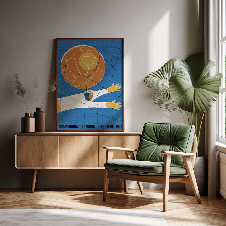 May include: A vintage poster featuring a stylised illustration of a football player diving to catch a ball in a net. The poster is framed and hanging on a wall in a living room setting. The text on the poster reads "Championnat du Monde de Football 1954".