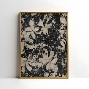 May include: A framed artwork featuring a floral pattern in black and beige. The design showcases overlapping flower shapes with a distressed, textured appearance. The artwork is encased in a gold-colored frame, adding a touch of elegance.