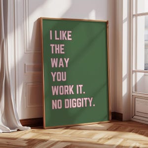 May include: A framed poster with the text "I LIKE THE WAY YOU WORK IT. NO DIGGITY." The text is in pink against a dark green background. The frame is gold, and the poster is leaning against a white wall.