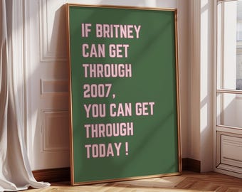 May include: A framed poster with a green background and pink text that reads, "IF BRITNEY CAN GET THROUGH 2007, YOU CAN GET THROUGH TODAY!". The frame is gold, and the poster is leaning against a white wall with a window and a wooden floor.
