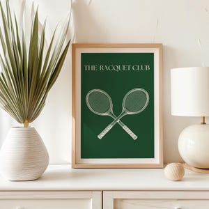 May include: A framed print with a green background and white text that reads "THE RACQUET CLUB". Two white tennis rackets are crossed in the center of the print.
