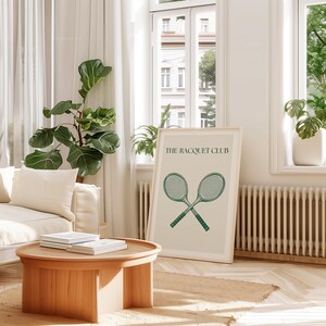 Puede incluir: Una impresi&oacute;n enmarcada con un fondo verde claro que presenta dos raquetas de tenis cruzadas y el texto "THE RACQUET CLUB".