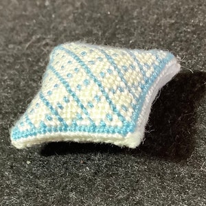 Puede incluir: Una pequeña almohada blanca y azul con un diseño de rombos. La almohada está hecha de un tejido suave y tejido.