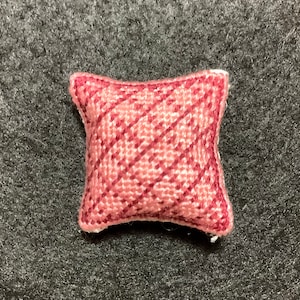 Puede incluir: Una pequeña almohada decorativa de color rosa con un patrón de rayas diagonales.