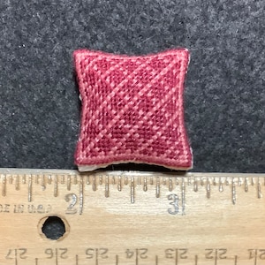 Puede incluir: Un pequeño cojín rojo y blanco con estampado, que mide aproximadamente 5 cm de ancho, se muestra en una regla.