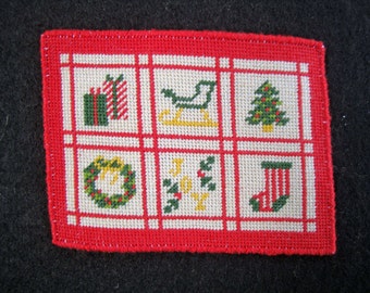 May include: A red and white needlepoint Christmas sampler with a white background and red border. The sampler features six different Christmas motifs: a wreath, a stocking, a Christmas tree, a sleigh, presents, and the word "JOY".