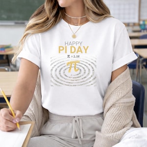 May include: White t-shirt with the text "HAPPY PI DAY" in gold lettering and the pi symbol. The shirt features a design of concentric circles with numbers. The shirt is short-sleeved.