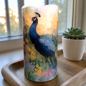 May include: A cylindrical LED candle featuring a vibrant peacock design. The candle's artwork depicts a blue peacock amidst colorful flowers. The candle is placed on a wooden tray, with a small succulent plant in a white pot nearby.