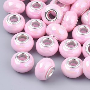 May include: A collection of pink ceramic beads with silver metal accents. The beads have a smooth, glossy finish and are designed for use in jewelry making.