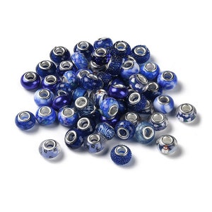 Puede incluir: Una colección de cuentas de vidrio azul y blanco con varios patrones. Las cuentas tienen un anillo de metal plateado alrededor del agujero central.
