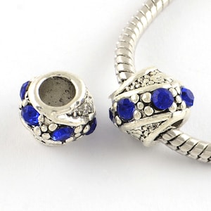 May include: Silver charm bead with blue crystal accents. The bead has a decorative design and is designed to fit on a charm bracelet.