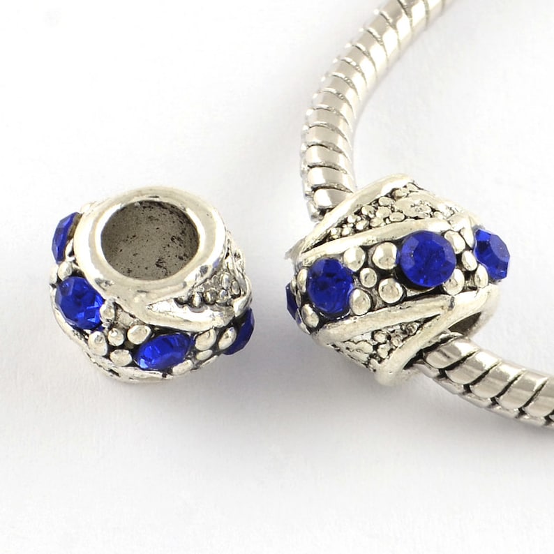 May include: Silver charm bead with blue crystal accents. The bead has a decorative design and is designed to fit on a charm bracelet.