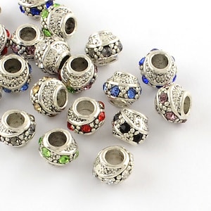 May include: A collection of silver-toned beads with various colored rhinestones. The beads are round and have a hole in the center for stringing.