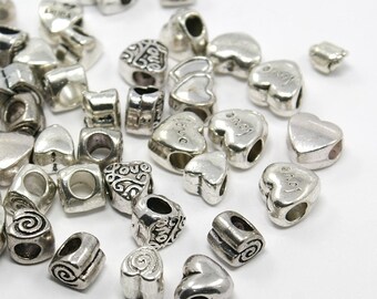 May include: A collection of silver-toned metal heart-shaped beads with various designs and inscriptions, including "love" and "angel".