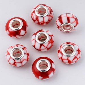 May include: Seven red and white glass beads with a checkerboard pattern. Each bead has a silver-colored metal core. The beads are round and have a hole through the center for stringing.