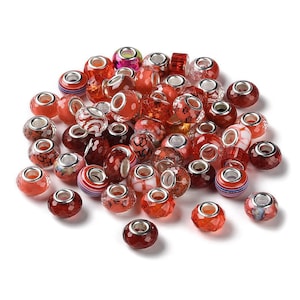 Pode incluir: Uma coleção de contas de vidro vermelho e transparente com núcleos de metal prateado. As contas variam em forma e design, incluindo estilos facetados, listrados e estampados. Algumas contas têm desenhos florais ou abstratos.