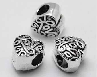 May include: Three silver-toned heart-shaped beads featuring a raised, embossed script that spells out the word love. Each bead has a central hole for threading, with a metallic finish and dark recessed areas that highlight the lettering and swirling patterns.