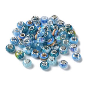 May include: A selection of blue glass beads with diverse patterns, such as stripes, swirls, and speckled designs. The beads feature silver-toned metal cores and are available in light and dark blue hues. Ideal for jewellery making.