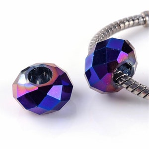 May include: Two faceted, iridescent beads in dark blue and purple hues. One bead is separate, the other is on a silver bracelet. The beads feature a geometric design and a central hole. The beads are suitable for jewellery making.