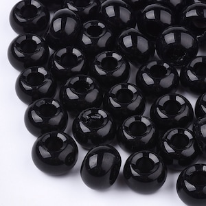 May include: A collection of glossy, black beads with a donut shape and a central hole. The beads are smooth and reflect light, suggesting a polished finish. These beads are suitable for jewelry making and crafting projects.