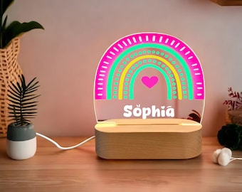 May include: A wooden night light with a pink, green, and yellow rainbow design and the name "Sophia" in white lettering. The rainbow has a heart in the center.