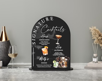 May include: A black arched sign with white text reading "Signature Cocktails." The sign features illustrations of cocktails and a dog wearing glasses. Cocktail names include "Espresso Martini," "Old Fashioned," and "Rosemary."