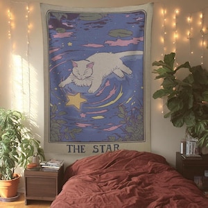 K&ouml;nnte beinhalten: Ein Schlafzimmer mit einem Wandteppich, der eine Katze und den Text "THE STAR" zeigt. Der Raum umfasst ein Bett mit einer bordeauxfarbenen Bettdecke, Pflanzen, Lichterketten und einen Nachttisch aus Holz.