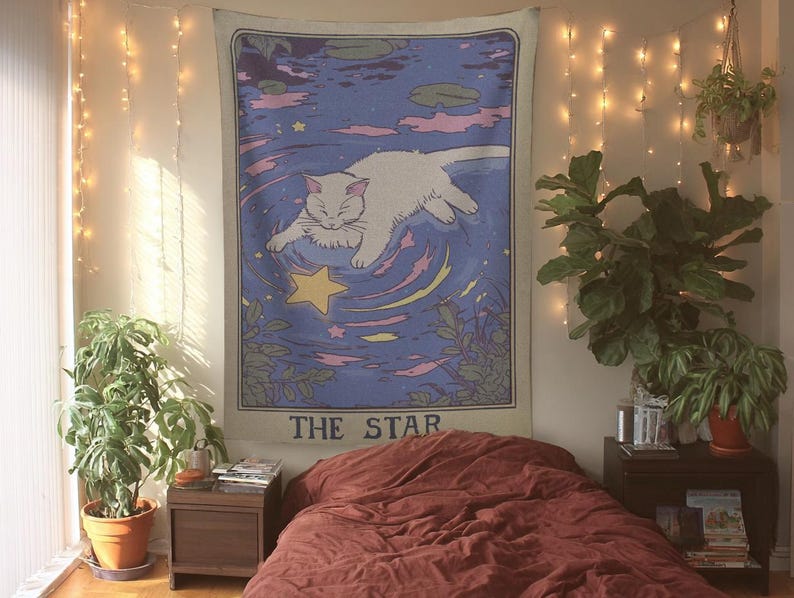 K&ouml;nnte beinhalten: Ein Schlafzimmer mit einem Wandteppich, der eine Katze und den Text "THE STAR" zeigt. Der Raum umfasst ein Bett mit einer bordeauxfarbenen Bettdecke, Pflanzen, Lichterketten und einen Nachttisch aus Holz.