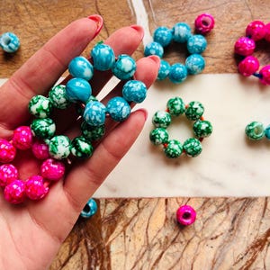 Pode incluir: Conjunto de scrunchies de cabelo de plástico marmorizado nas cores azul, verde e rosa. Os scrunchies estão dispostos sobre uma superfície branca.