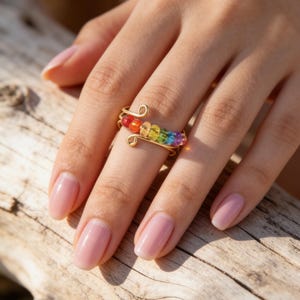May include: A gold-toned wire ring featuring a row of small, multicoloured beads arranged in a rainbow sequence. The wire is coiled at both ends, creating an open-ended design that wraps around the finger, showcasing red, orange, yellow, green, blue, and purple beads.