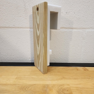 May include: A wooden wall mount with a white plastic bracket. The mount has a natural wood grain finish and a small hole in the top.