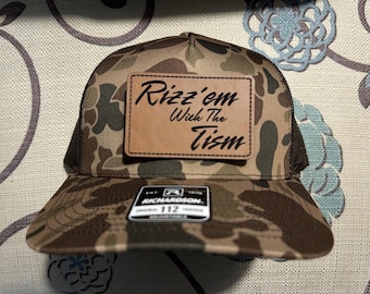 May include: Camouflage baseball cap with a brown mesh back and a curved brim. A rectangular leather patch displays the text "Rizz'em With The Tism". The cap has a Richardson 112 tag.