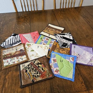 Puede incluir: Una colección de once posavasos cuadrados de tela con varios patrones y colores. Los diseños incluyen estampados florales, geométricos y abstractos. Cada posavasos está bordeado con una tela contrastante.