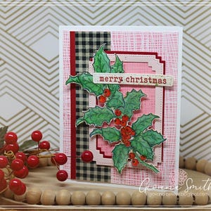 May include: A handmade Christmas card featuring a holly branch with red berries and the text "merry christmas." The card has a pink background with a plaid and textured design. The card is on a wooden tray with red berries.