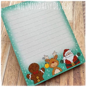 May include: A lined notepad with a teal border and snowflake accents. The bottom of the notepad features cartoon illustrations of a gingerbread man, a reindeer with a gold ornament, and Santa Claus. The text "SweetMissDaisy Designs" is at the top.