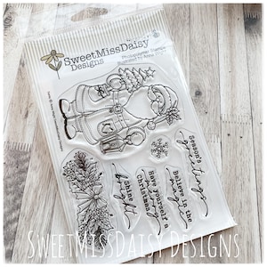 May include: A clear plastic package of Sweet Miss Daisy Designs photopolymer stamps featuring a line art illustration of Santa Claus holding a lantern, a holly branch, a snowflake, and the text Season's greetings, Believe in the magic, Have yourself a merry Christmas, and Shine bright.