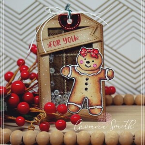May include: A handmade Christmas gift tag featuring a gingerbread person with a red bow. The tag has a plaid background and the words "FOR YOU" on a banner. Red berries and wooden beads are also in the image.