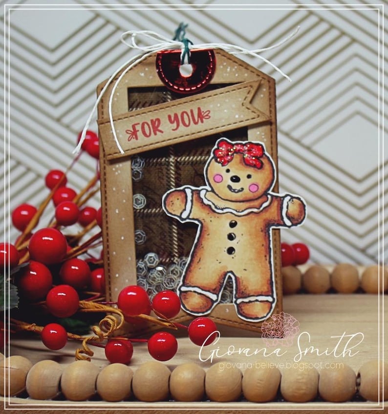 May include: A handmade Christmas gift tag featuring a gingerbread person with a red bow. The tag has a plaid background and the words "FOR YOU" on a banner. Red berries and wooden beads are also in the image.