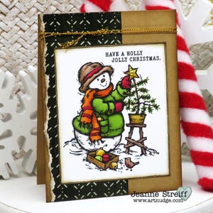 May include: A Christmas card featuring a snowman decorating a small tree. The snowman wears a brown hat, orange scarf, and green coat. The card has the text "Have a Holly Jolly Christmas." A small bird and a box of ornaments are also shown.