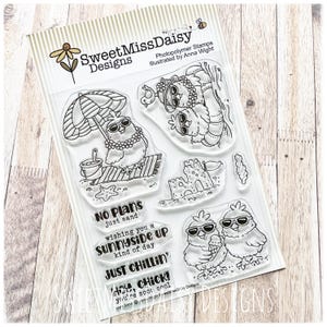 May include: A set of clear photopolymer stamps by SweetMissDaisy Designs featuring illustrations of chicks in sunglasses at the beach, a sandcastle, and phrases including NO PLANS just sand, WISHING YOU A SUNNYSIDE UP KIND OF DAY, JUST CHILLIN'.