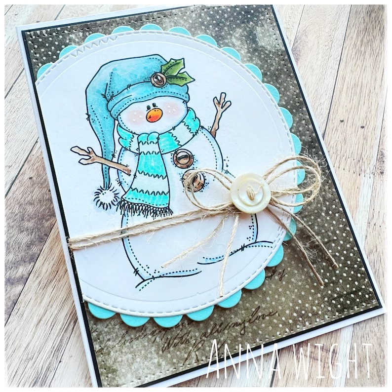 May include: A handmade Christmas card featuring a snowman with a blue hat, a striped scarf, and a holly sprig. The card has a scalloped edge and is decorated with twine and a button.